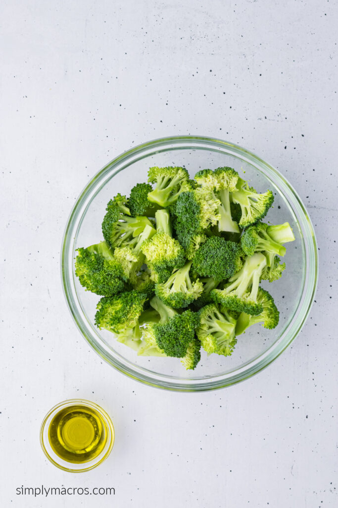 Broccoli in a bowl with a side of olive oil to be mixed together. 