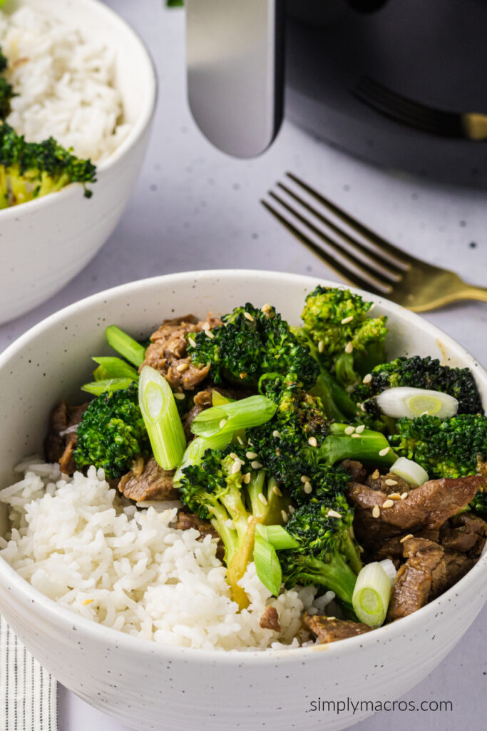 Air fryer beef and broccoli served over white rice in a bowl and topped with sesame seeds and chopped green onions. 