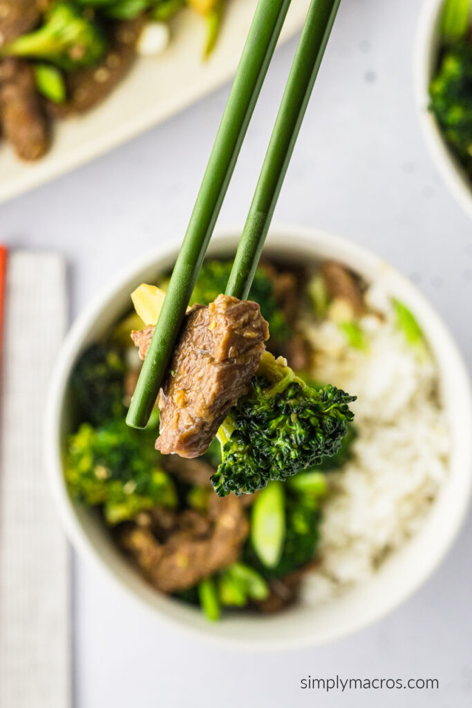 Bite shot of beef and broccoli in a pair of chopsticks. 