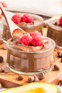 Acovado chocolate mousse being scooped with a wooden spoon with raspberries on top.