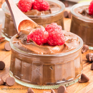 Acovado chocolate mousse being scooped with a wooden spoon with raspberries on top.