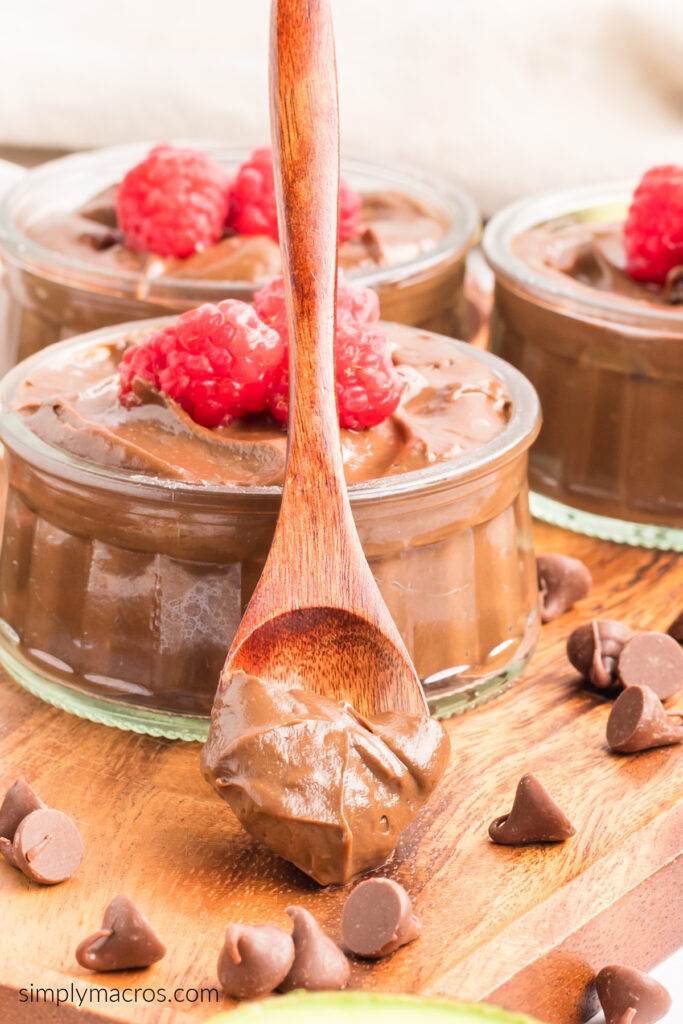 Spoonful of chocolate avocado mousse leaning against a bowl with mousse, and topped with fresh fruit. 