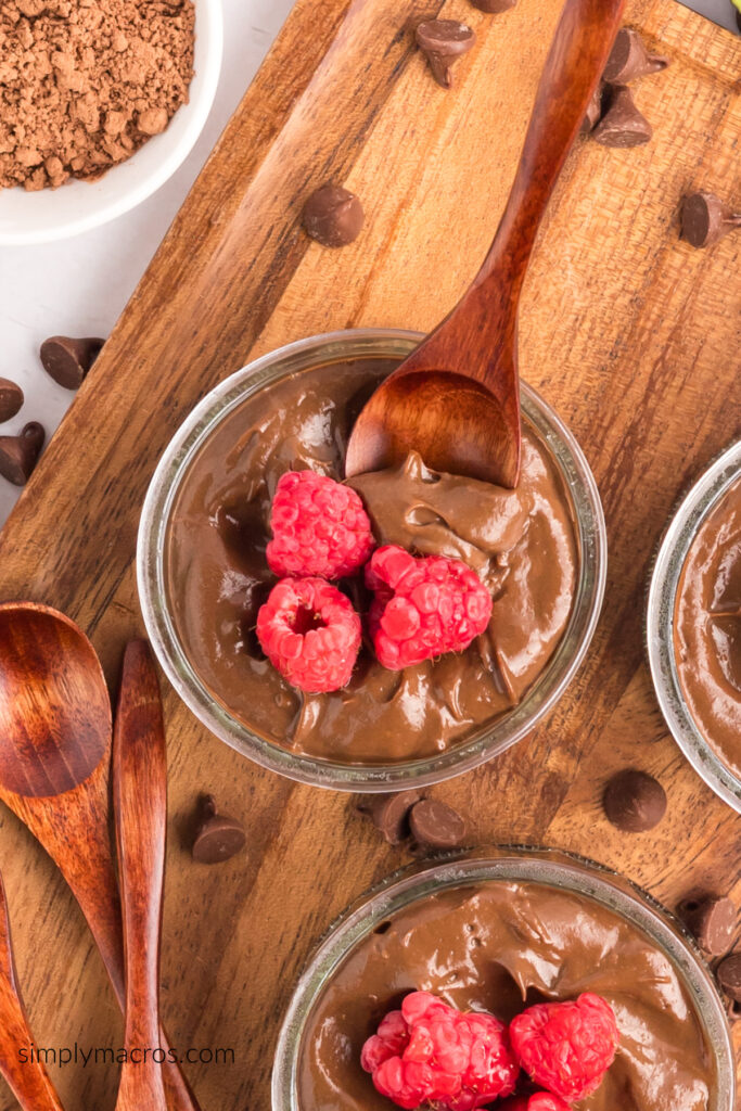 Avocado chocolate mousse topped with fresh raspberries and with a wooden spoon taking a bite.