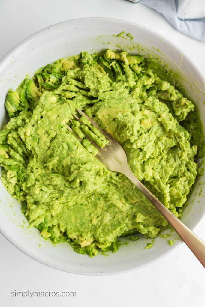 avocados mashed with a fork in a white bowl. 