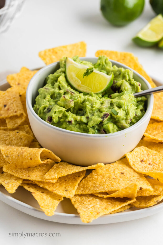 Easy guacamole dip in a white bowl surrounded by chips. Topped with a slice of lime. 