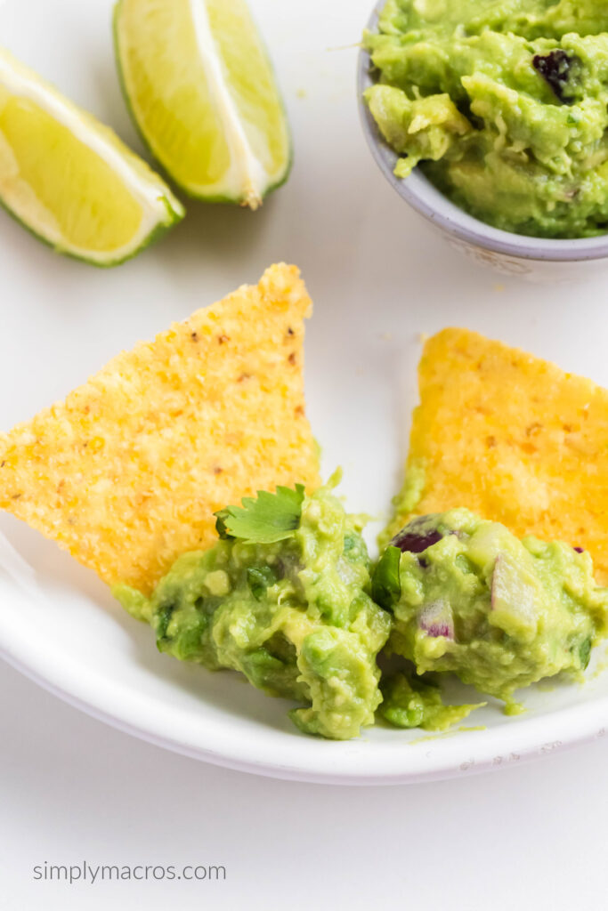 Close up shot of guacamole dip on chips, on a white plate. 