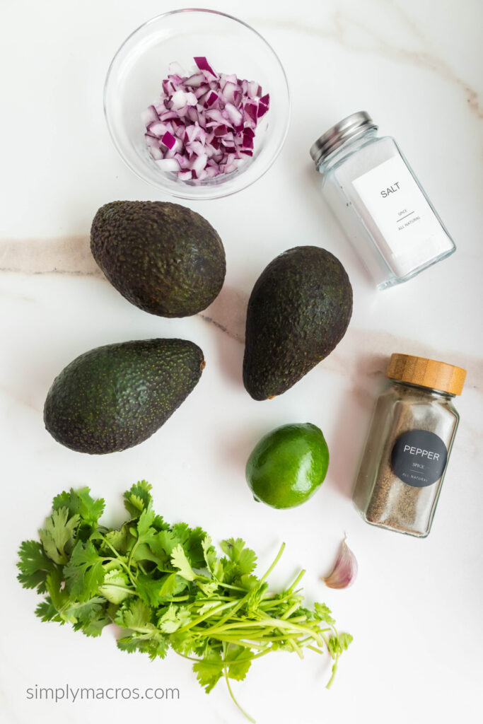 3 ripe avocados, salt, pepper, cilantro, lime, clove of garlic, and dices onion on a white table top. 