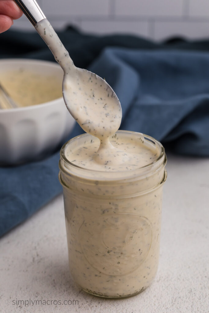 Low calorie ranch dresing made with light mayo, plain greek yogurt, almond milk, and seasonings being scooped out of a jar with a spoon.