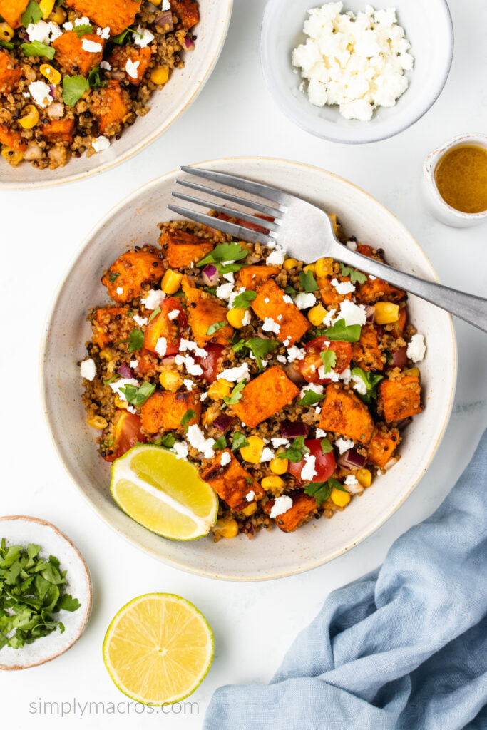 Overhead photo of a quinoa sweet potato bowl with feta cheese sprinkled on top, a lime wedge on the side, and a fork for serving.  