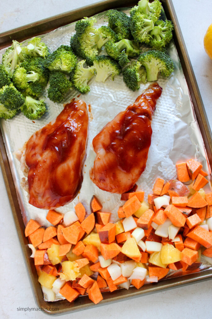 Vegetables, chicken, and broccoli on a sheet pan, ready to be placed into the oven. 