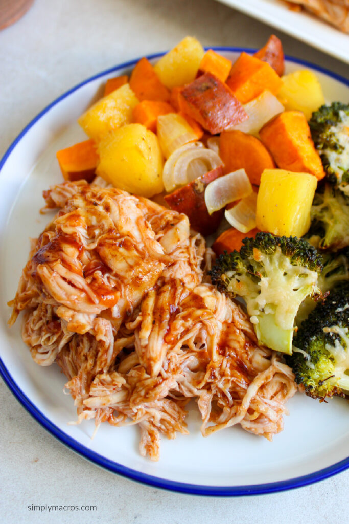 Close up of shredded sheet pan bbq chicken on a plate with roasted vegetables. 