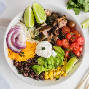 Steak burrito bowl with lime wedges, ready to eat.