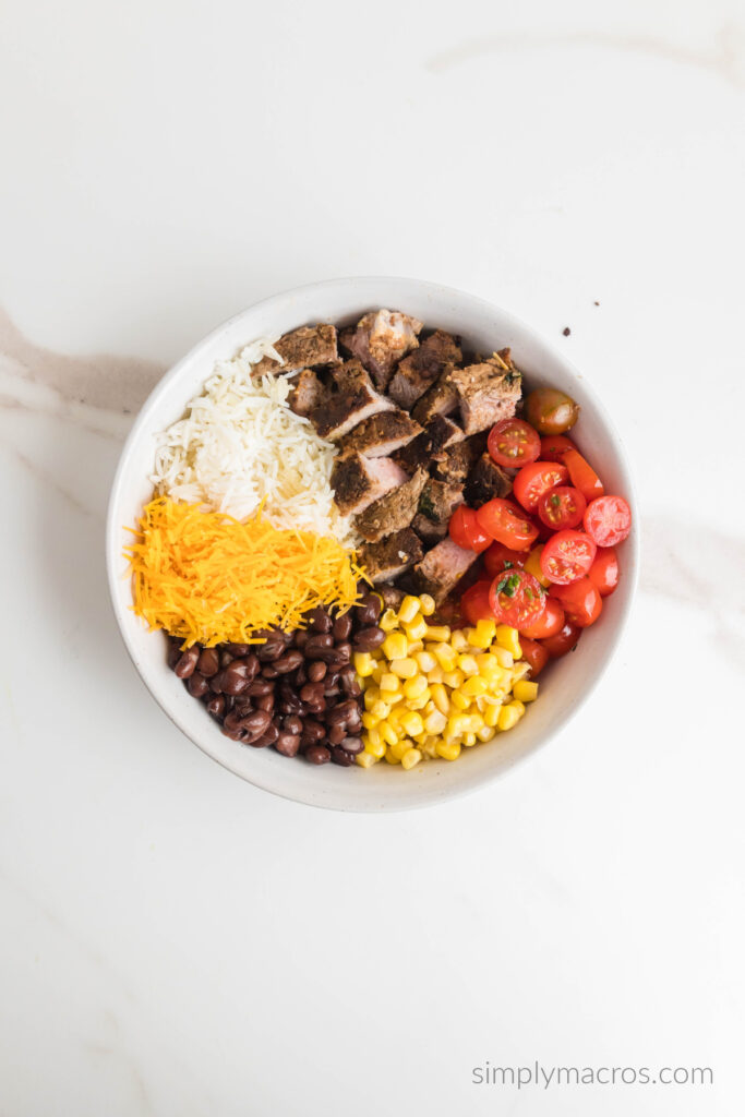 steak, rice, cheese, tomatoes, beans, and corn placed into a bowl. 