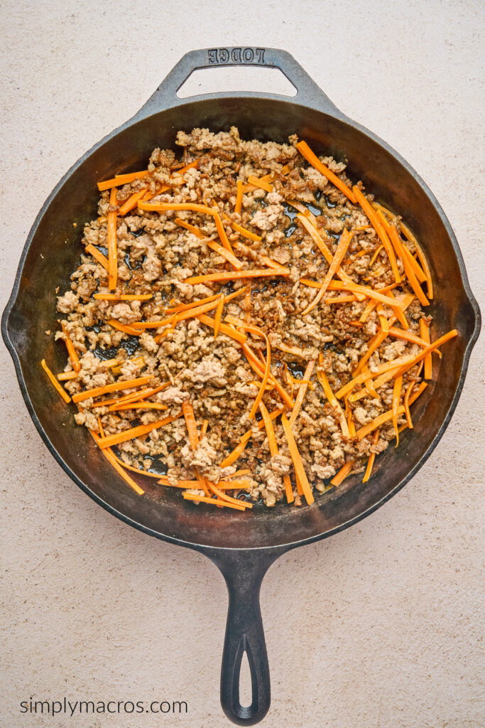 Ground beef with carrot matchsticks in the bottom of a skillet. 