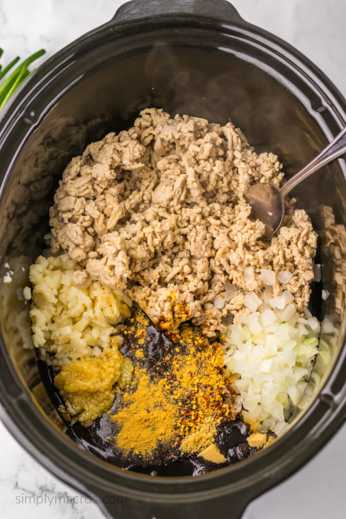 Cooked ground chicken, hoisin sauce, soy sauce, rice wine vinegar, sesame oil, onion, garlic, ginger, red pepper flakes, brown sugar, and water chestnuts in a slow cooker, ready to mix and cook. 