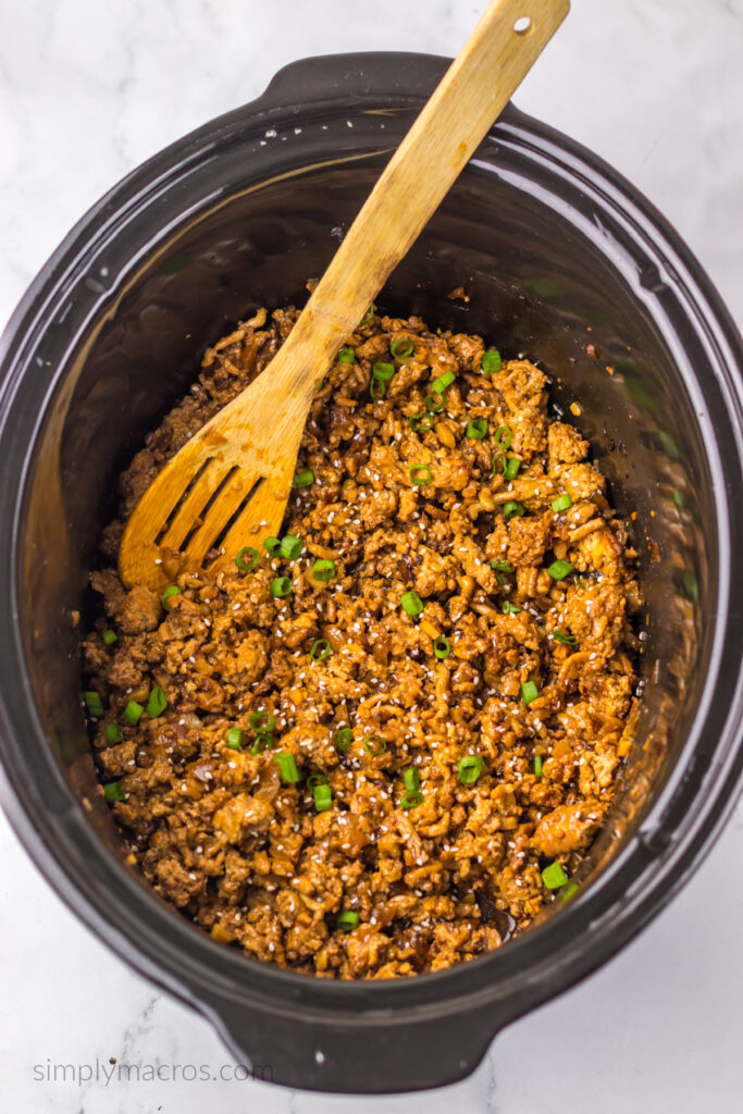 Seasoned ground chicken in a slow cooker topped with sesame seeds and scallions to be used in lettuce wraps to create copycat PF Chang's lettuce wraps. 