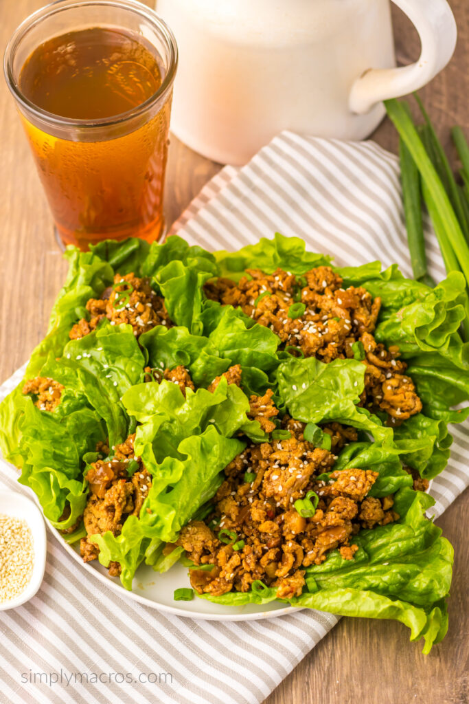 Copycat PF Chang's chicken lettuce wraps topped with scallions and sesame seeds served on a white plate. 