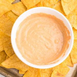 Cottage cheese queso in a white bowl on a tray with tortilla chips.