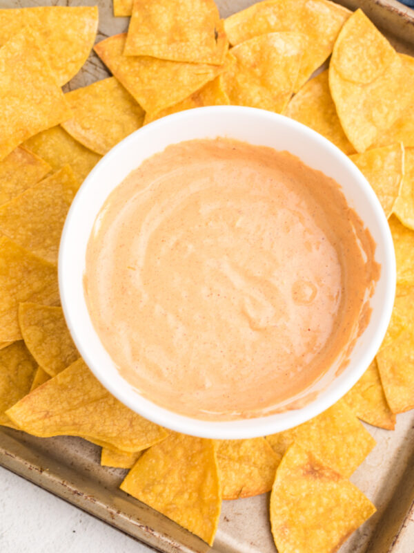 Cottage cheese queso in a white bowl on a tray with tortilla chips.