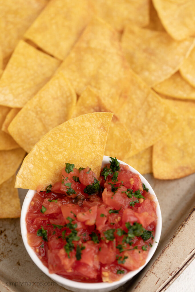 Close up photo of healthy homemade tortilla chips and a side of salsa for dipping. 