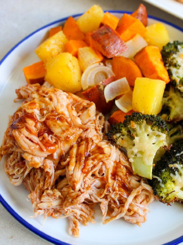 Sheet pan BBQ chicken shredded and served on a plate with vegetables.