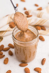 Creamy homemade almond butter being spooned from a jar.