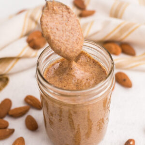 Homemade almond butter in a jar with a spoon pulling some out for serving.