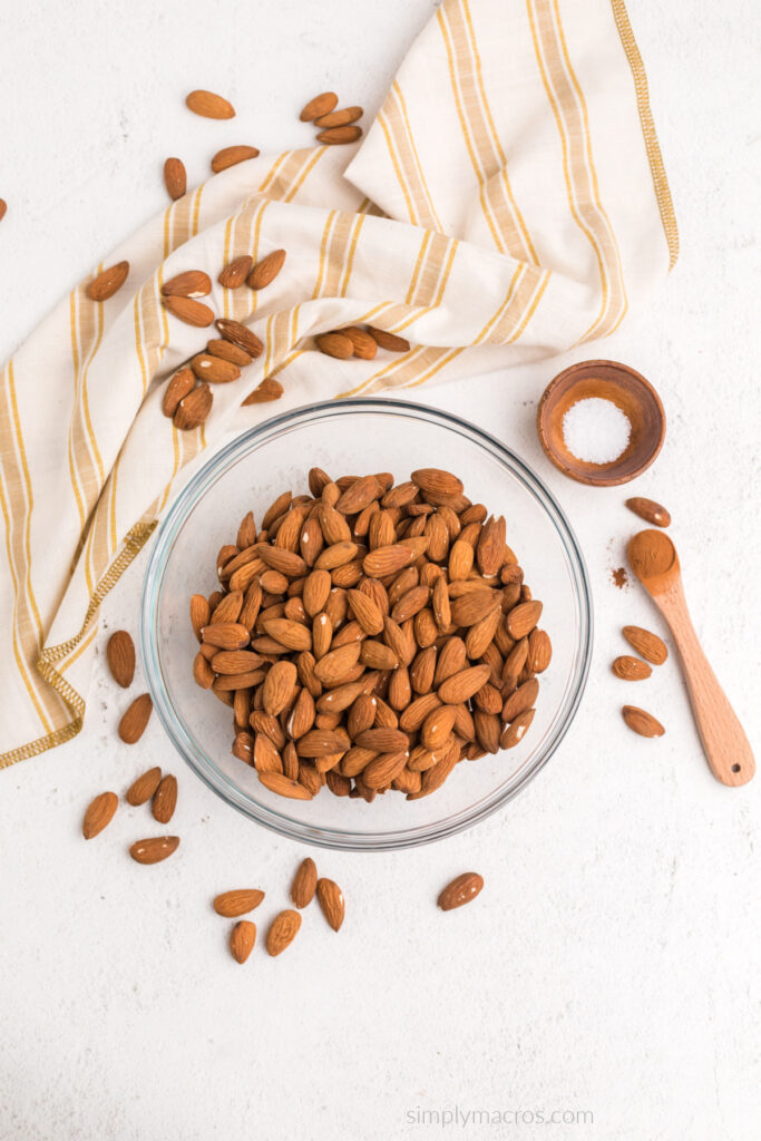 Fresh raw almonds in a bowl, with a small bowl of salt, and a small spoon with cinnamon. 