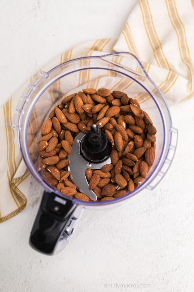 Roasted almonds in the bottom of a food processor fitted with an s blade. 