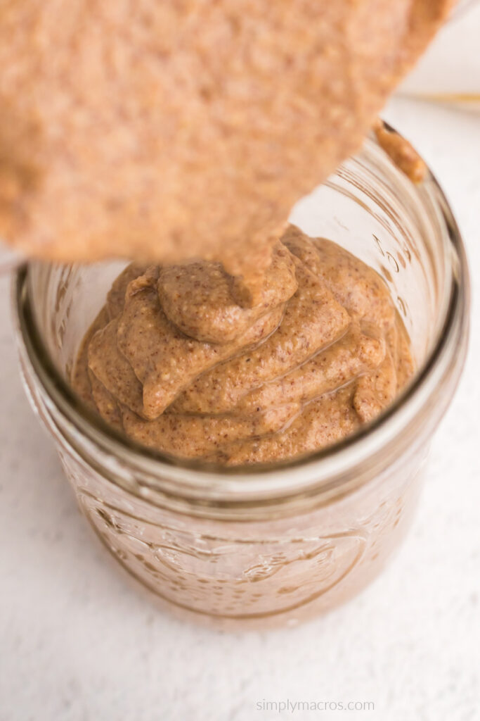 Almond butter being poured from a food processor into a jar for refrigerating and storing. 