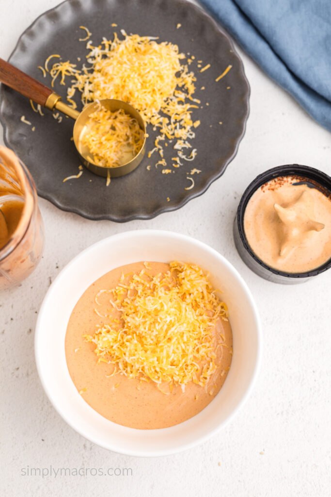 Cottage cheese and taco seasoning blended and added to a bowl, topped with freshly shredded cheddar jack cheese, ready to heat. 