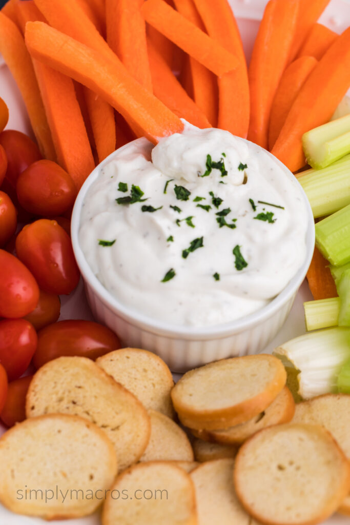 Cottage cheese ranch dip surrounded by carrots, tomatoes, celery, and bagel crisps. 