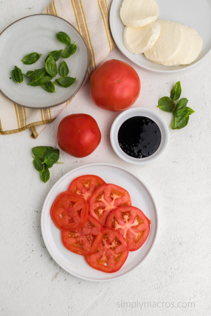 Plates with sliced tomato and sliced mozzarella, as well as a plate with fresh basil leaves. 