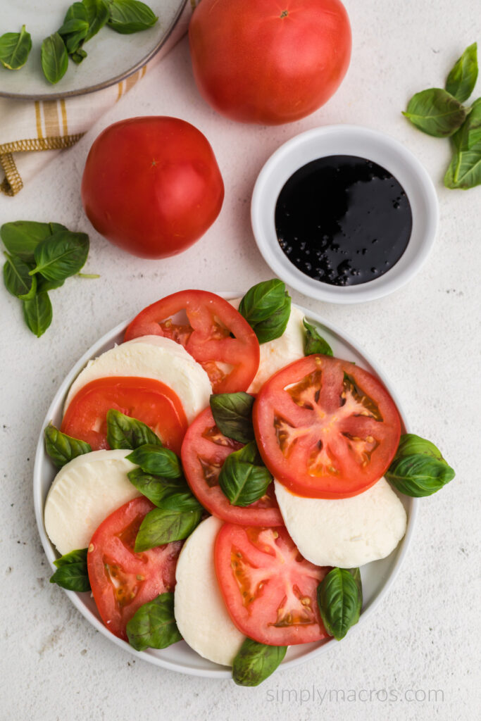 Sliced heirloom tomatoes and sliced mozzarella cheese alternated on a plate with fresh basil leaves throughout. 