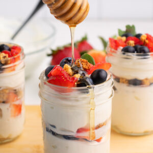 Greek yogurt parfait with honey being drizzled on top.