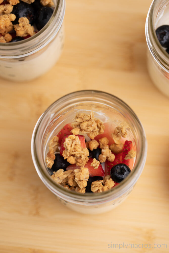 Overhead photo of Greek Yogurt Parfait in jars being layered with fruit and granola. 