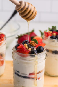 Greek yogurt parfait being drizzled with honey.