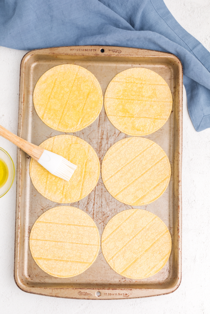 Tray with corn tortillas and a brush, adding olive oil to the tortillas before cutting and baking. 