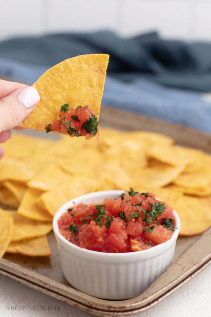 Hand holding a homemade tortilla chip that's been dipped in salsa. 