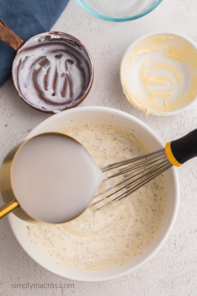 Almond milk being poured into a bowl to thin out the ingredients to make a low calorie ranch dressing. 