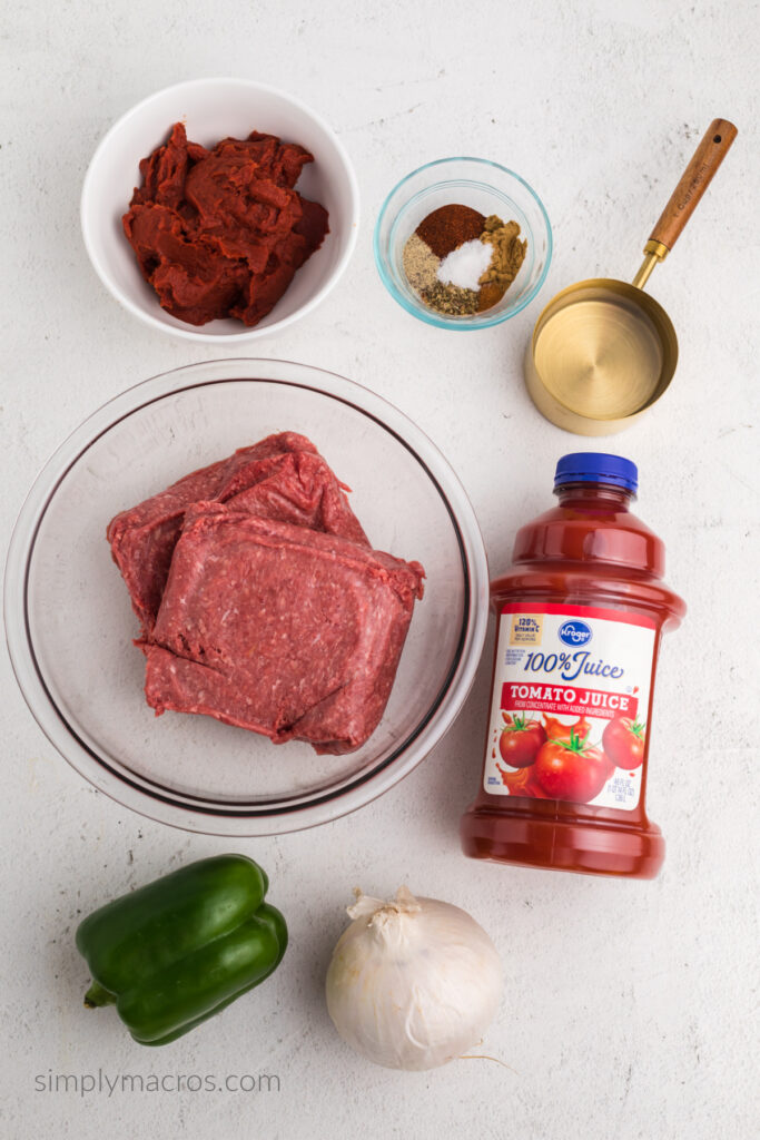 Ingredients on a white table top to make no bean chili. Ground beef, tomato paste, seasonings, water, tomato juice, onion, and bell pepper.