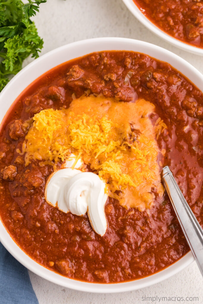 Close up photo of no bean chili with freshly shredded cheddar cheese and sour cream on top. 