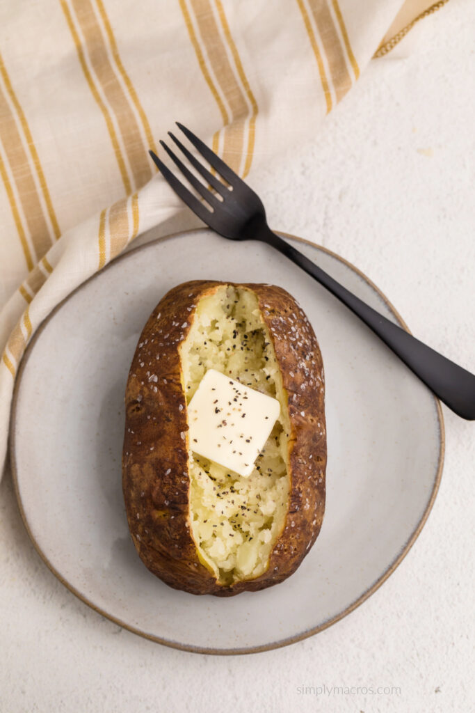 Air fried baked potato opened and with added butter and pepper, on a plate with a fork. 