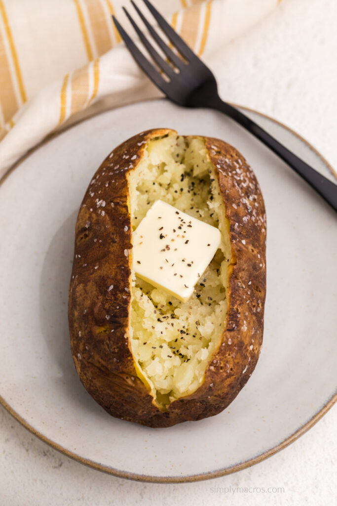 Close up of air fried baked potato on  a plate, opened with butter and pepper, and ready to eat. 