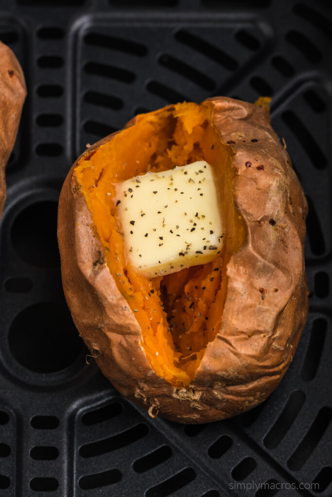 Baked sweet potato in the air fryer basket with a sliced of butter and a dash of seasoning.