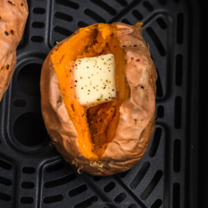 Baked sweet potato in the air fryer basket with a slice of butter and seasoning on top.