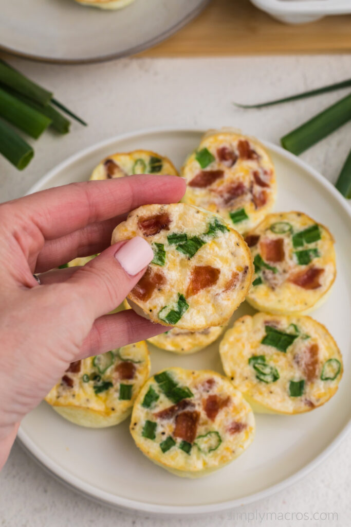 Copycat Starbucks Egg White bites are on a white plate with a hand holding one of the bites to eat. 