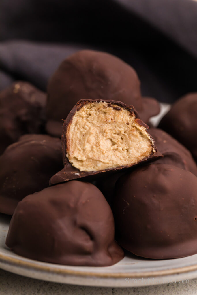 High protein peanut butter balls stacked on a plate, with one cut in half on top. 