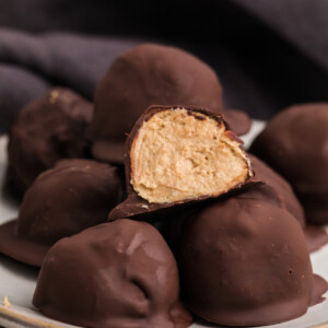 Chocolate covered protien balls stacked on a plate with one cut in half on top.