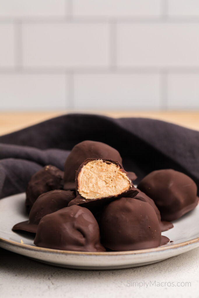 High protein peanut butter balls stacked on a plate, one cut in half on top. 